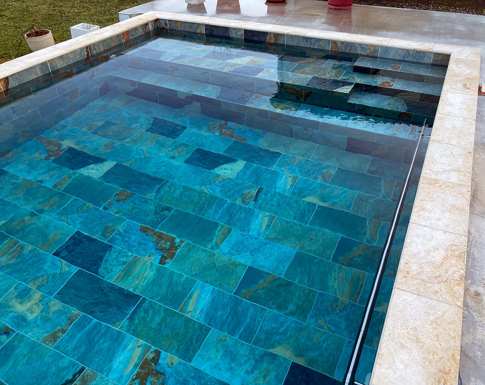 Piscine avec carreaux turquoise et bord en pierre.