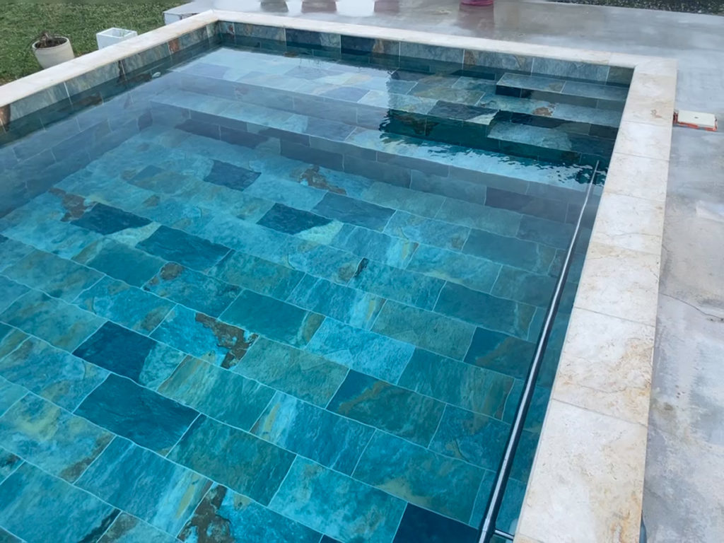 Piscine avec carrelage bleu et bordure blanche.