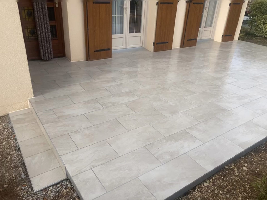 Terrasse carrelée devant porte-fenêtres en bois.