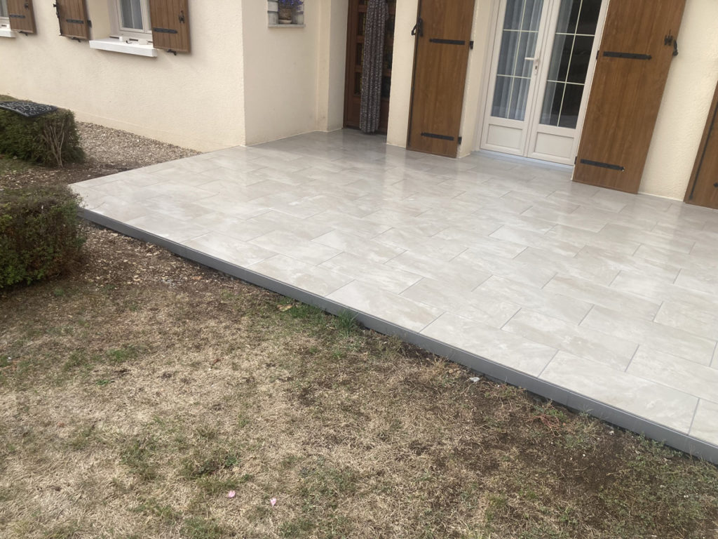 Terrasse carrelée devant une maison beige.