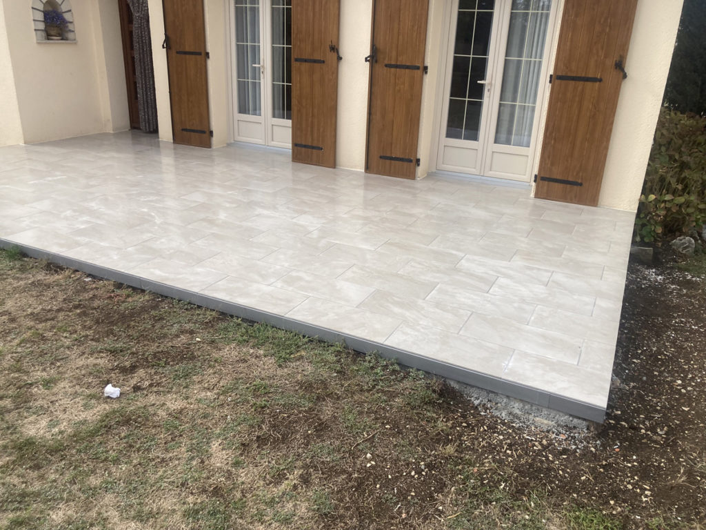 Terrasse carrelée neuve devant maison, portes en bois.
