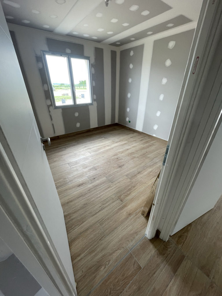 Chambre vide avec parquet et murs plâtrés.