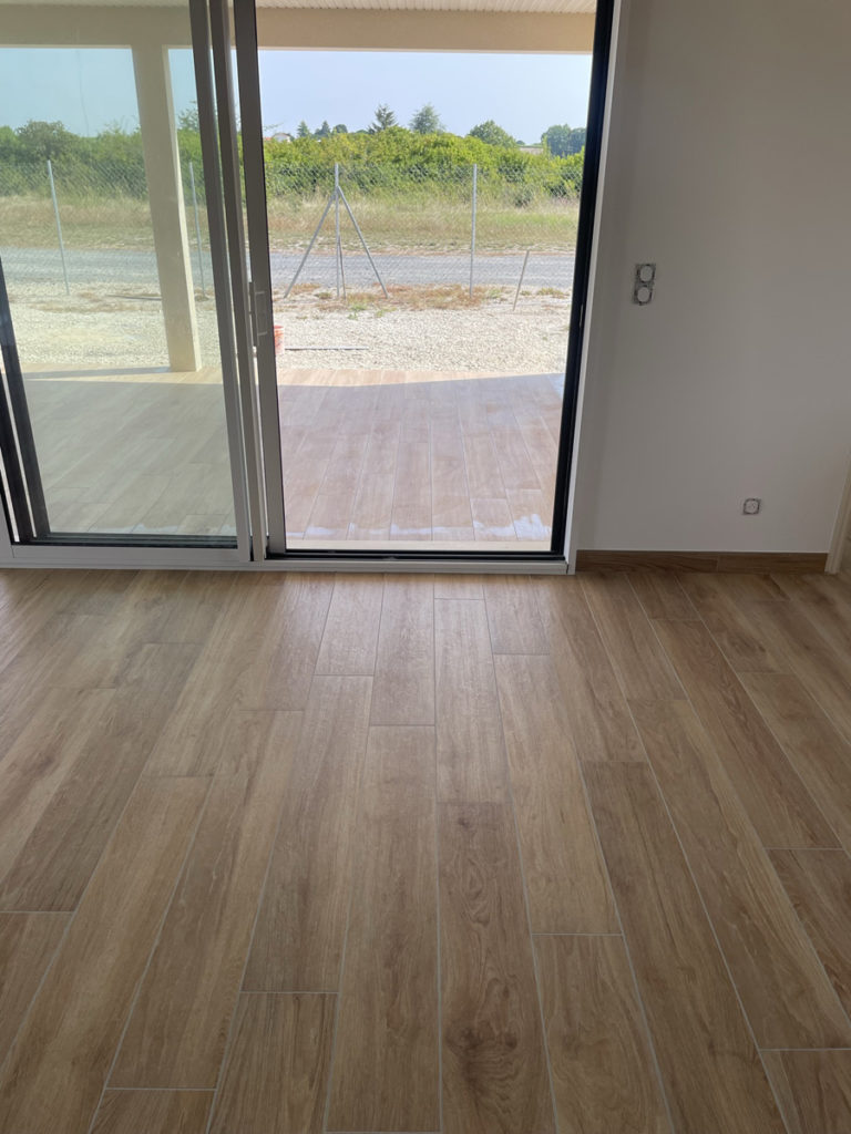 Salle vide avec parquet et portes-fenêtres ouvertes.