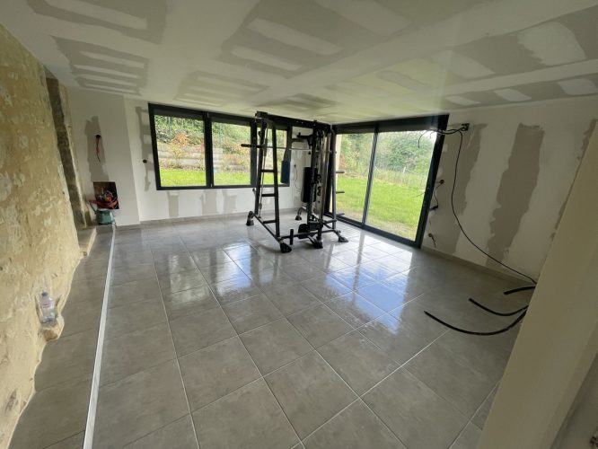 Salle de sport avec équipement, fenêtres et vue jardin.