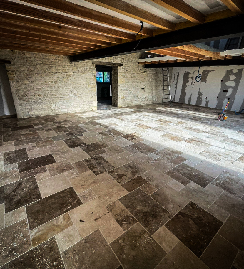 Salle avec carrelage en pierre et poutres apparentes.